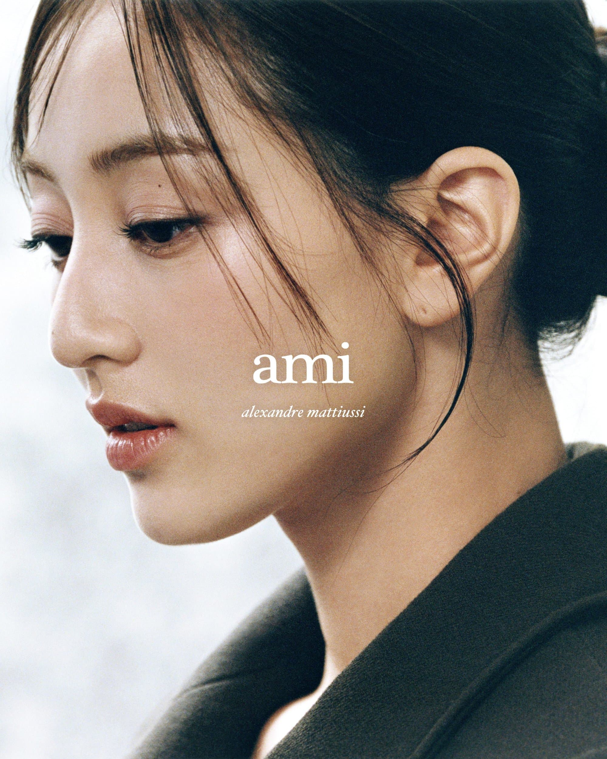 Close-up portrait of a woman with dark hair and neutral makeup looking in profile against a light background for Ami.