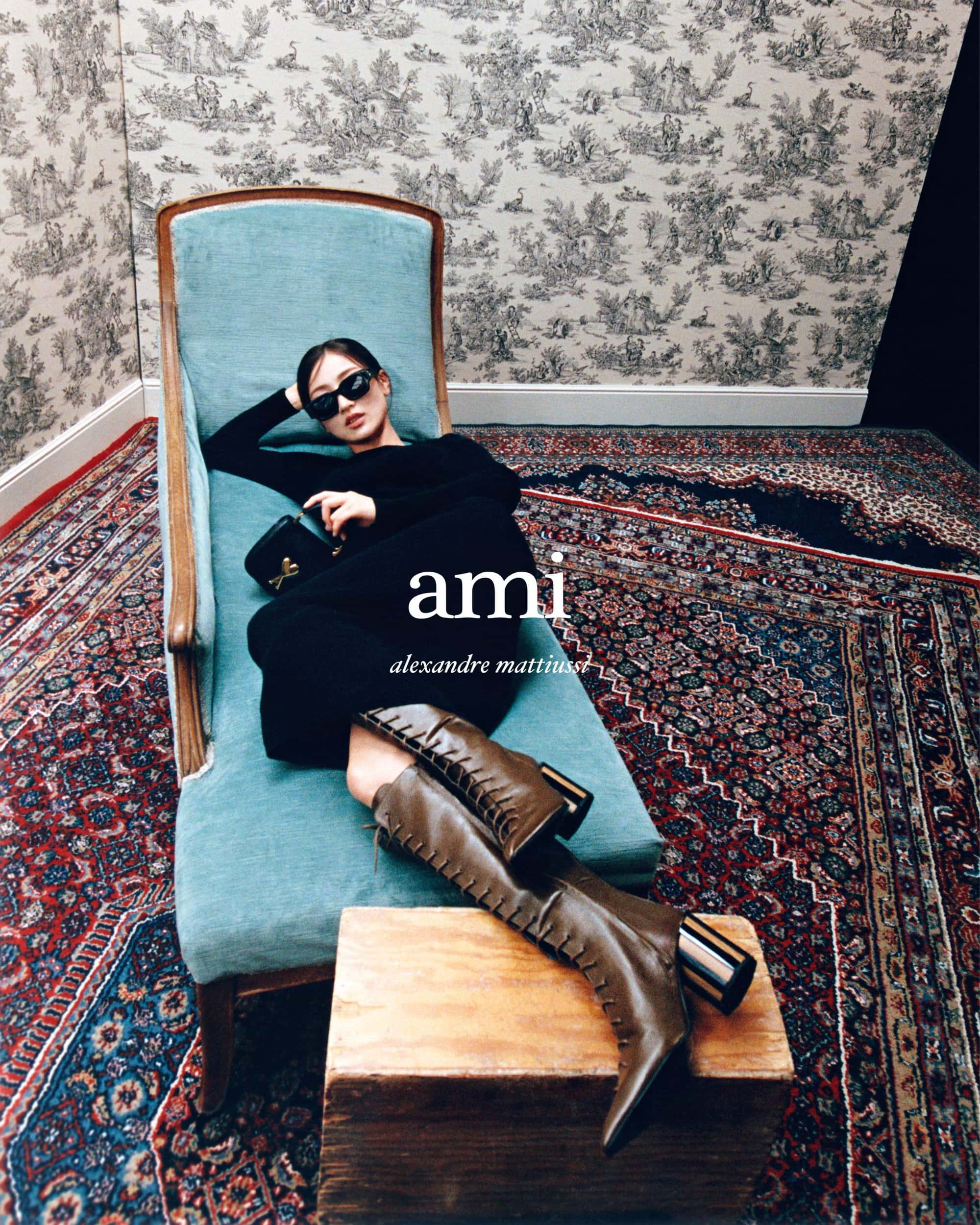 Model wearing black clothing and brown boots reclining on a turquoise chaise lounge in an ornate room