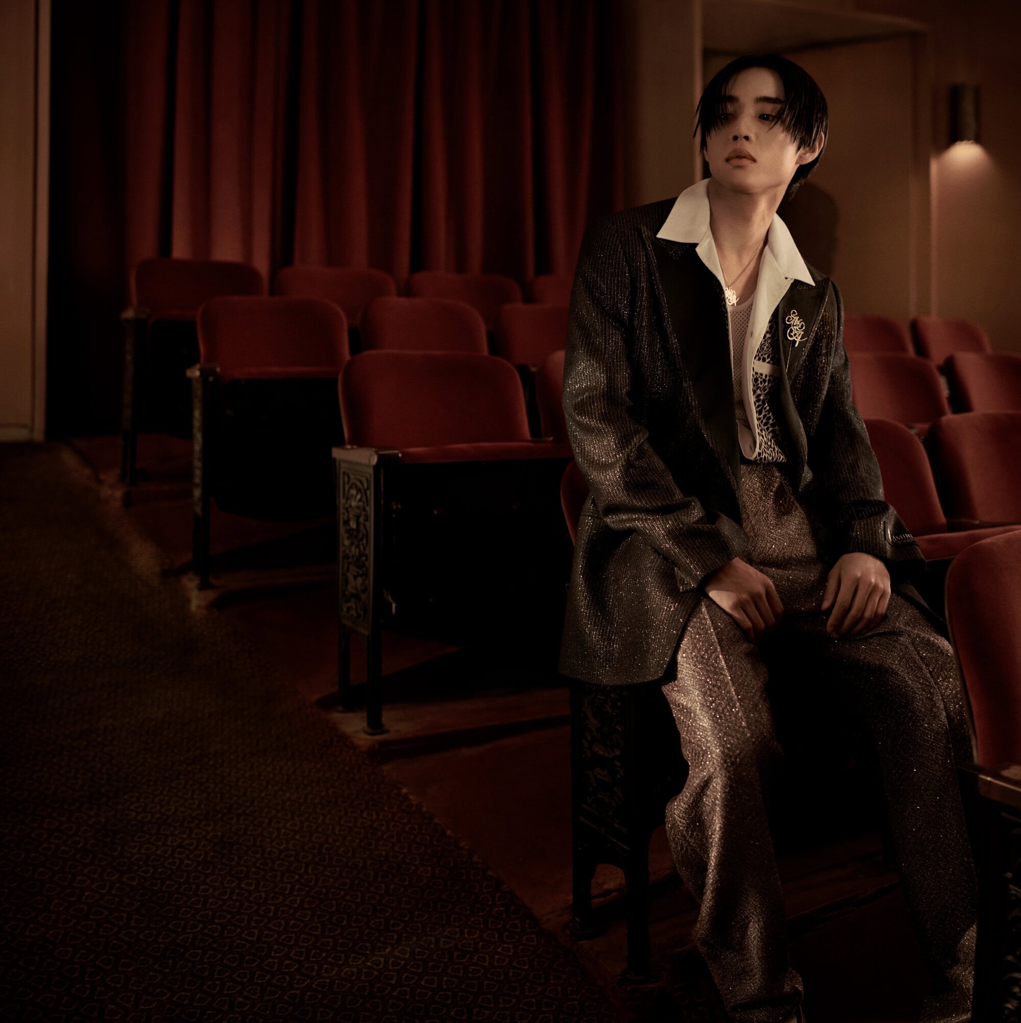 Young man in a dark textured suit seated in a red velvet cinema theater chair