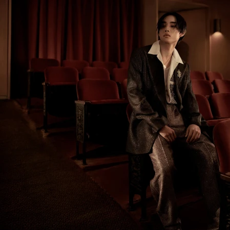 Young man in a dark textured suit seated in a red velvet cinema theater chair