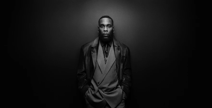 Burna Boy in a dark suit and leather jacket against a black studio background for BOSS Fall 2024 campaign
