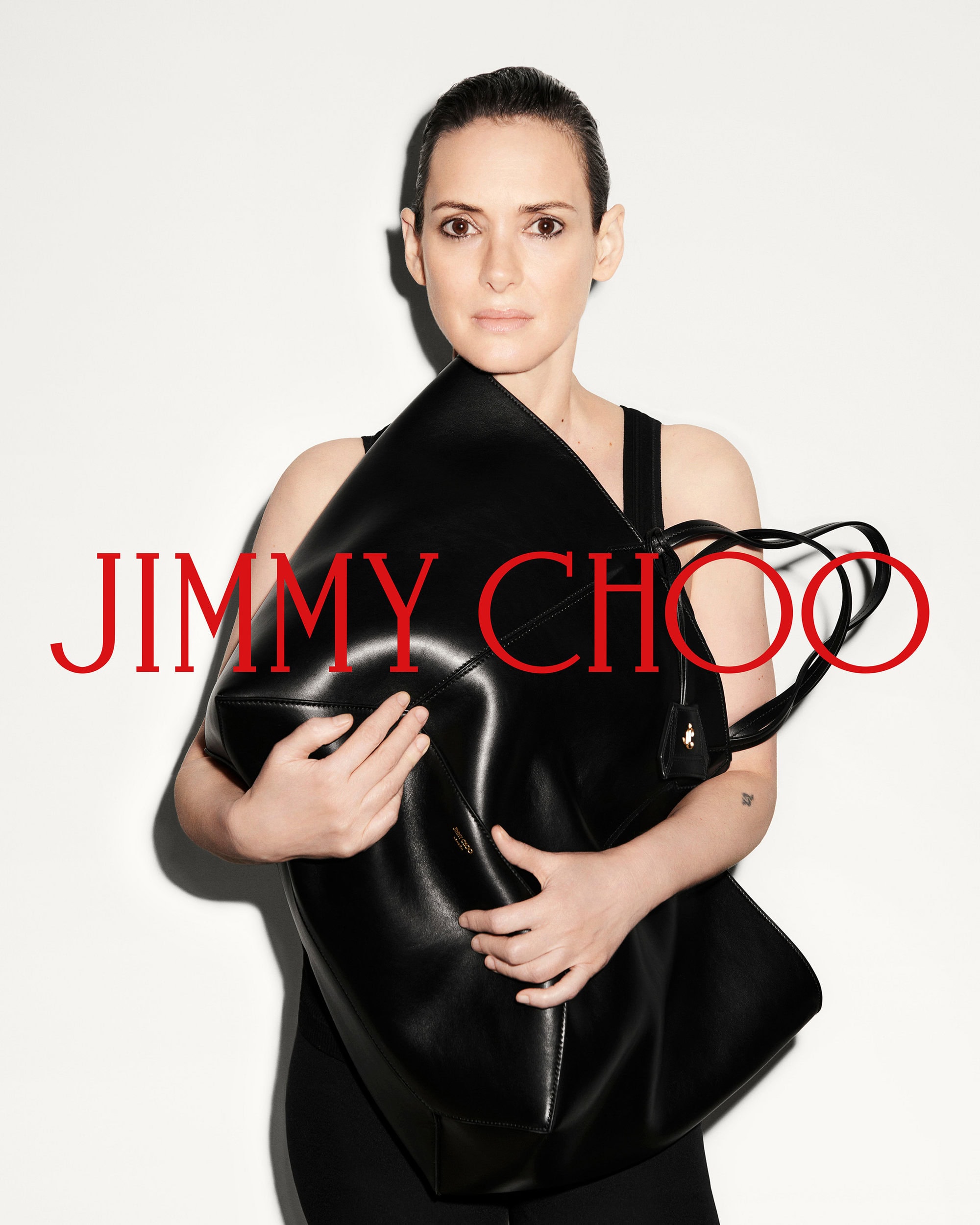 Winona Ryder holding a large black leather tote bag against a white studio background for Jimmy Choo Fall 2024 campaign