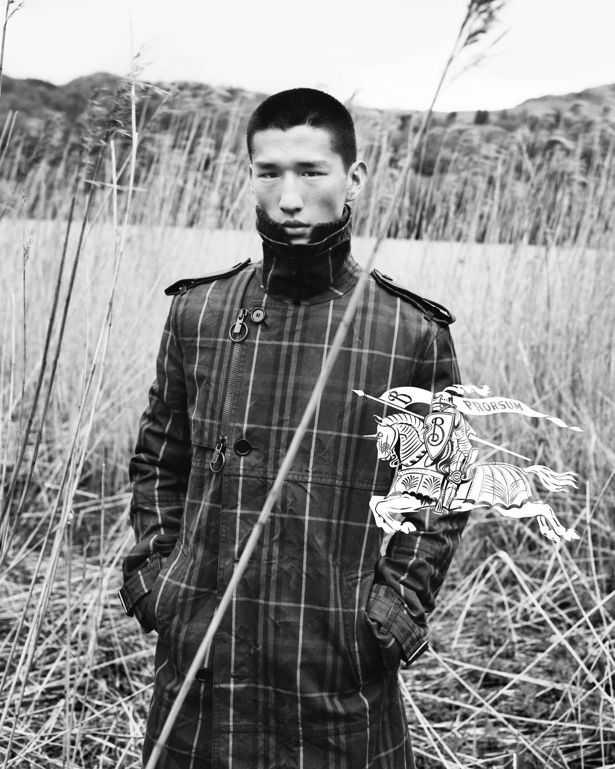 Man wearing a plaid coat posing among tall grasses in an outdoor field for Burberry Winter 2024 ad campaign