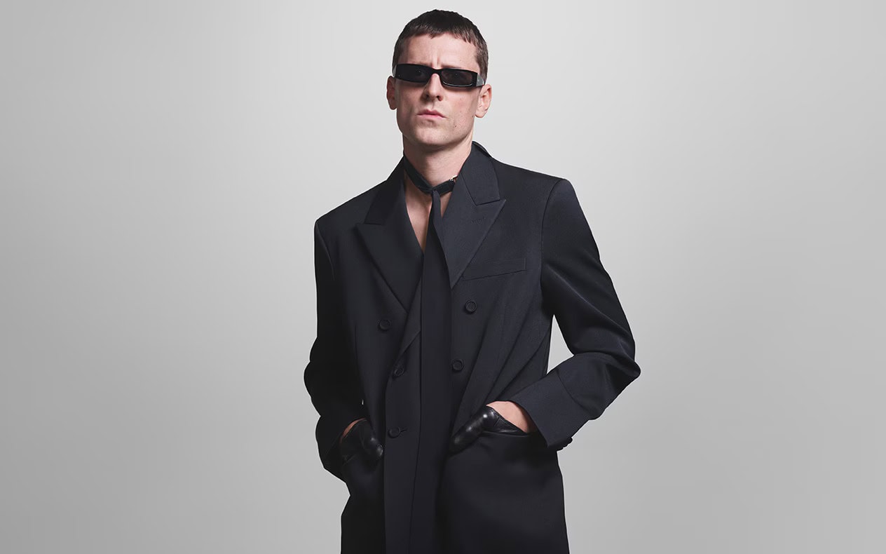 Man wearing dark sunglasses and a black suit jacket against a plain grey background for Gucci Eyewear Fall 2024