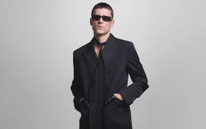 Man wearing dark sunglasses and a black suit jacket against a plain grey background for Gucci Eyewear Fall 2024