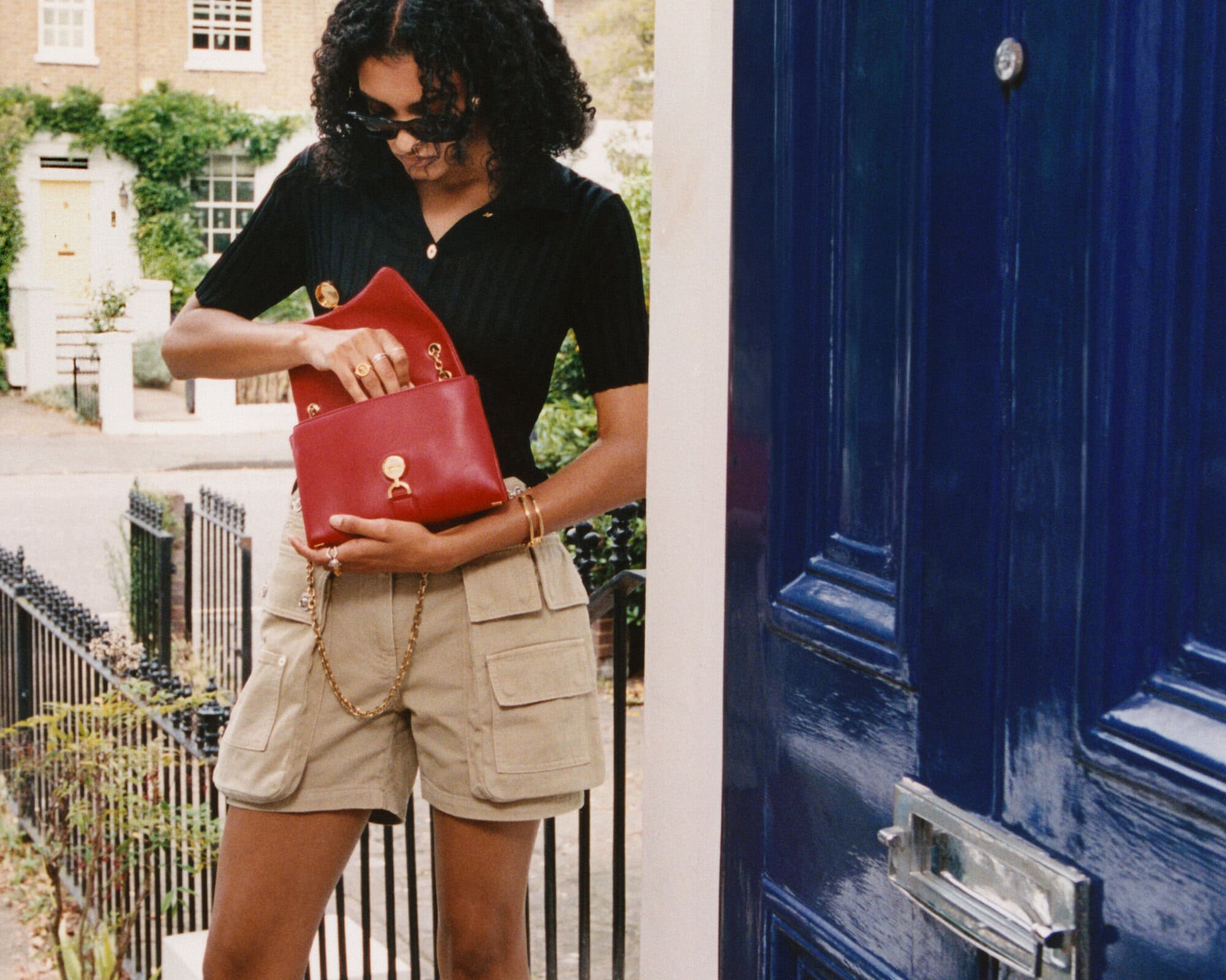 Woman wearing a black top and beige cargo shorts holds a red handbag outside