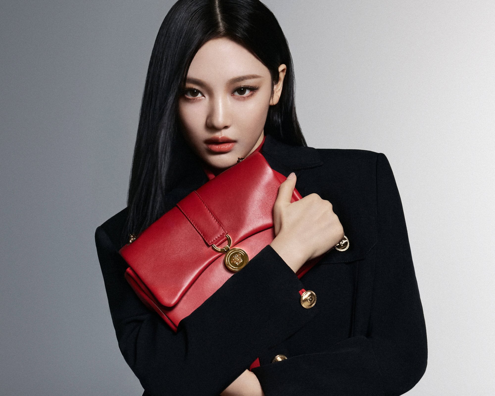 Woman with long black hair wearing a black jacket holding a red leather handbag