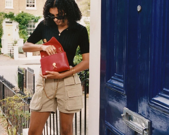 Woman wearing a black top and beige cargo shorts holds a red handbag outside