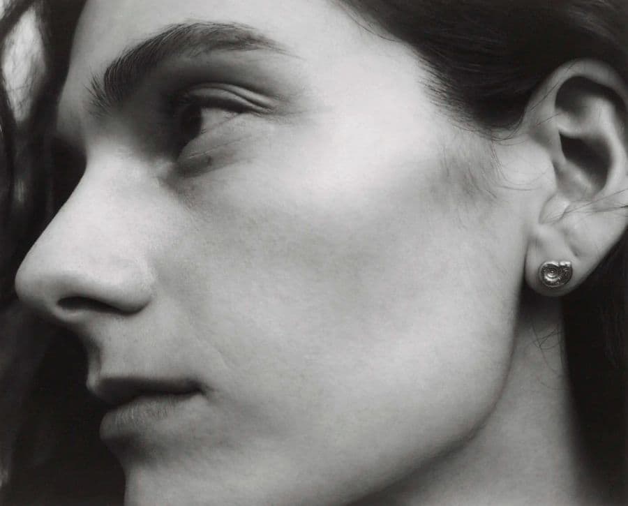 Close-up profile portrait of a model wearing a small metallic stud earring against an outdoor background
