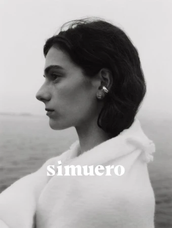 Profile portrait of a woman wearing silver earrings and an off-white textured garment outdoors near water for Simuero