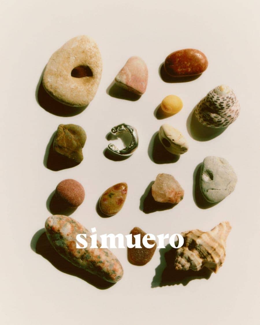 A collection of various smooth stones, shells, and a single silver ring arranged flat on a light cream surface.