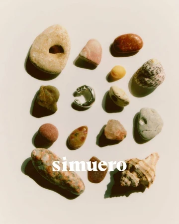 A collection of various smooth stones, shells, and a single silver ring arranged flat on a light cream surface.