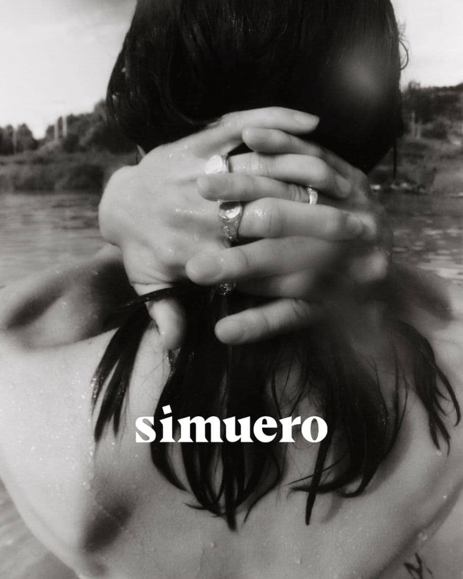Close-up of hands clasped behind dark hair wearing silver rings against an outdoor water background with Simuero text overlay.