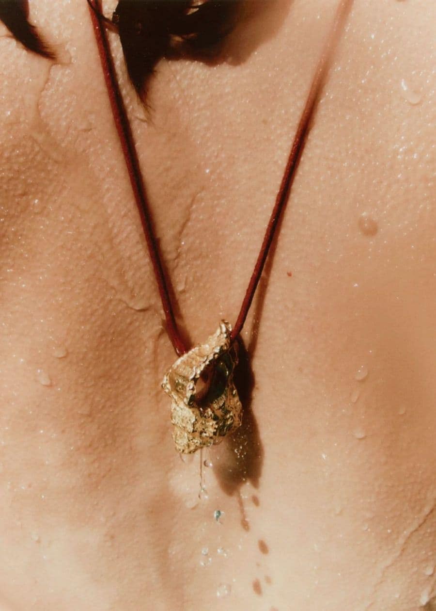 Close-up of a gold pendant necklace on a wet human back for Simuero Marea Collection 2024 campaign