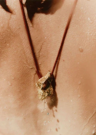 Close-up of a gold pendant necklace on a wet human back for Simuero Marea Collection 2024 campaign