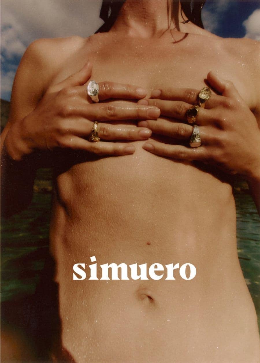 Close-up of a model wearing multiple gold and silver rings with wet skin outdoors against a natural water background.