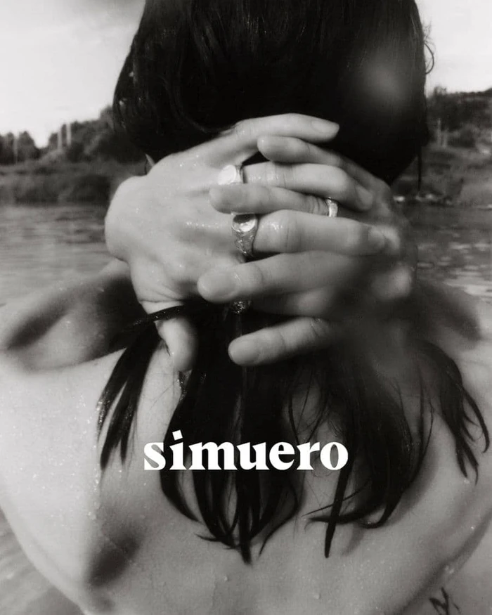 Close-up of hands clasped behind dark hair wearing silver rings against an outdoor water background with Simuero text overlay.