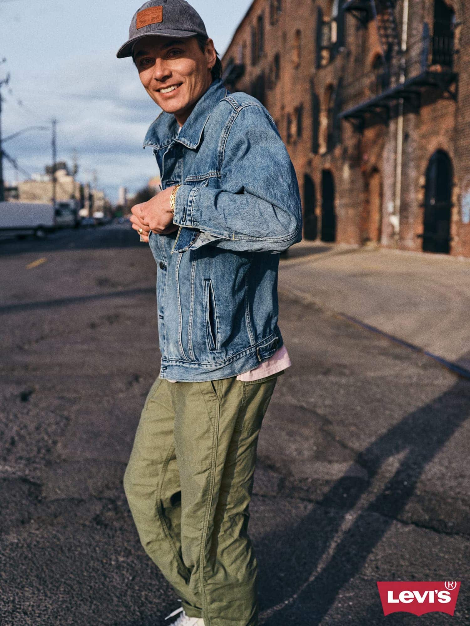 Man wearing a denim jacket and baseball cap smiling outdoors on a city street for Levi's Back At It campaign.