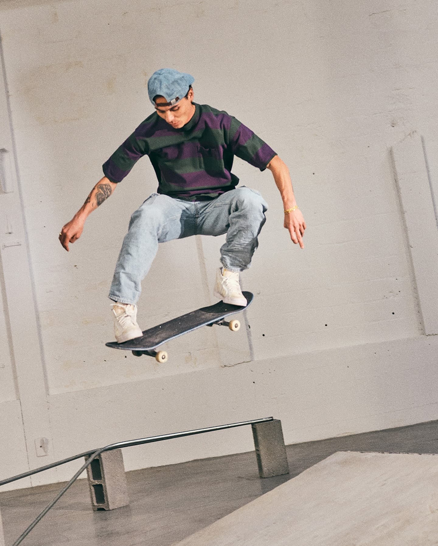 Skater mid-air performing a trick over a rail inside an industrial indoor space wearing a striped t-shirt and light jeans