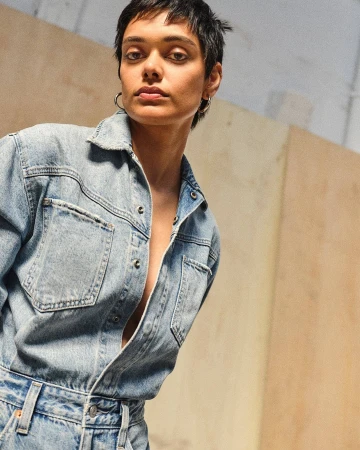 Model with short dark hair wearing a light blue denim shirt against wooden panels for Levi's