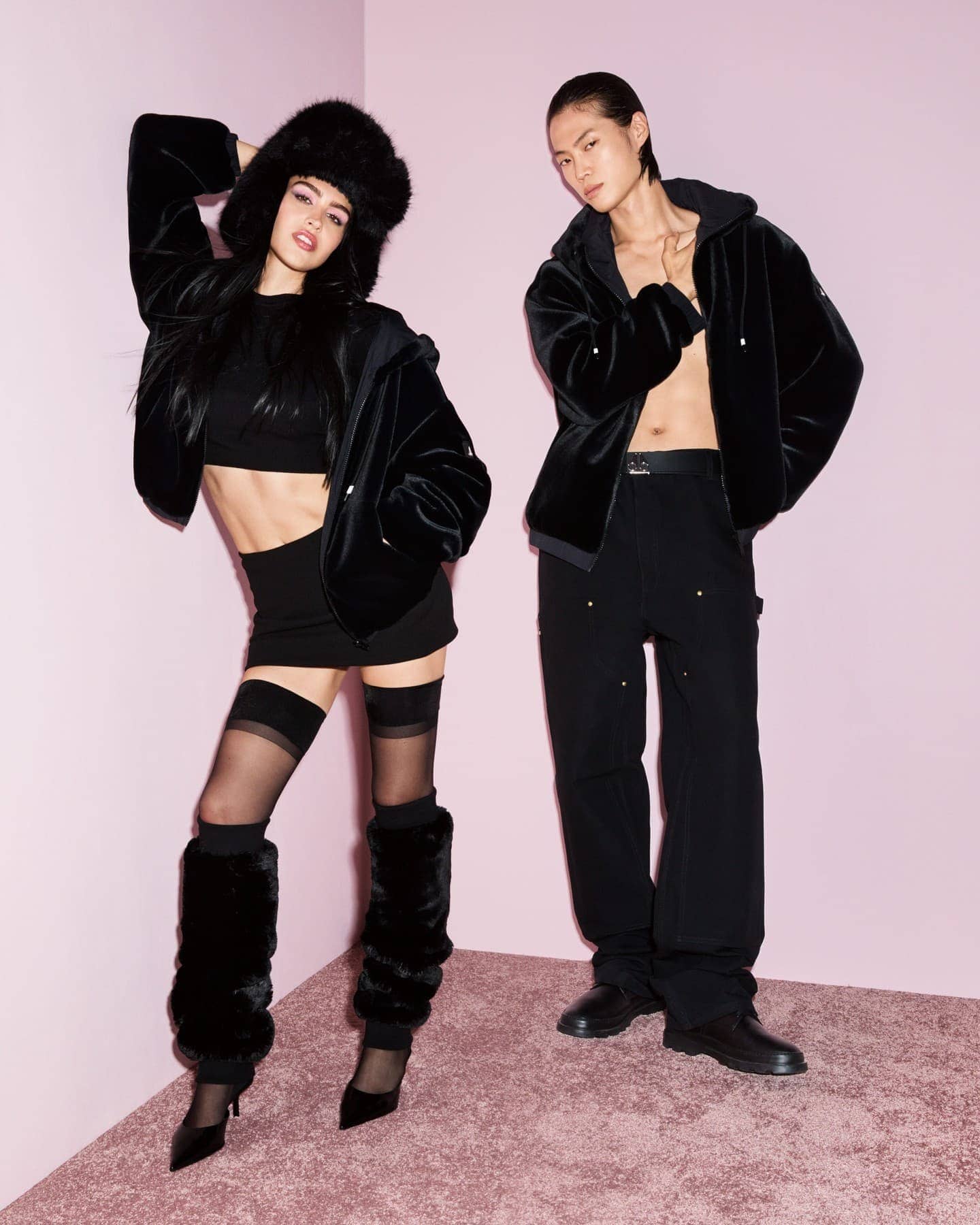 Two models wearing black outerwear posing against a pink set background for Moose Knuckles Fall 2024 campaign