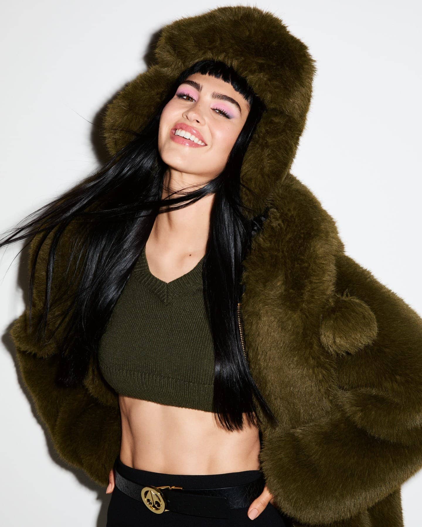 Model wearing an olive green faux fur hooded jacket and crop top against a neutral white background