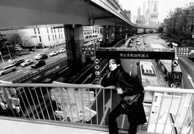 Model leaning against a metal railing on an elevated urban overpass overlooking a busy highway in Shanghai