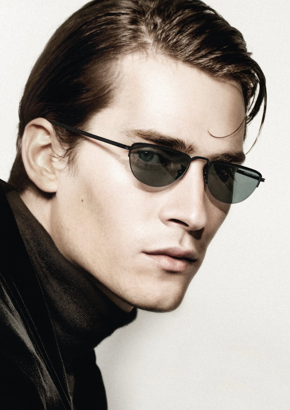Close-up portrait of a male model wearing dark sunglasses and a black turtleneck against a white background for Giorgio Armani