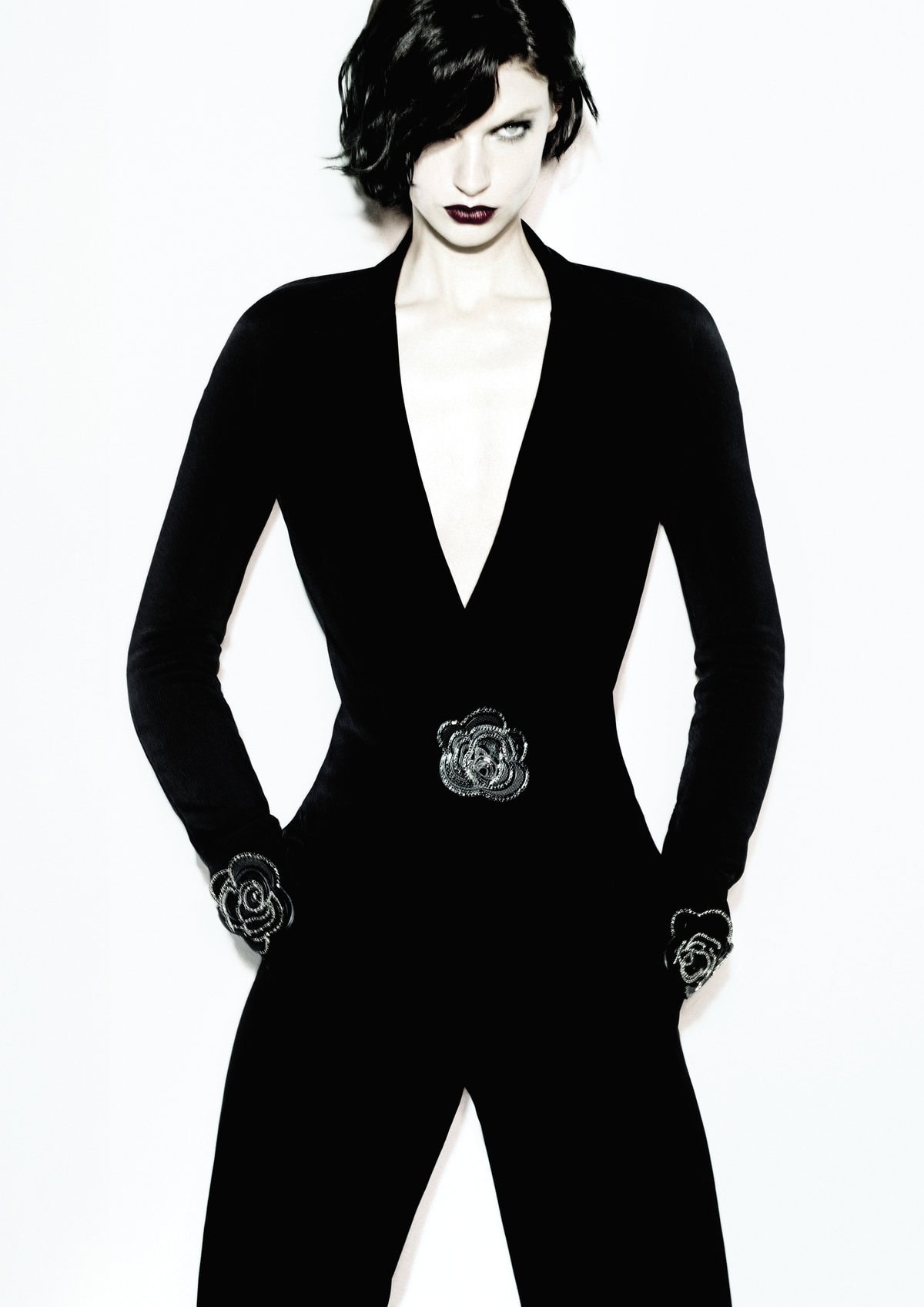 Model in dark V-neck jumpsuit with floral embellishments posing against a plain white background for Giorgio Armani