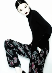 Model wearing a black top and floral patterned trousers against a clean white seamless studio background.