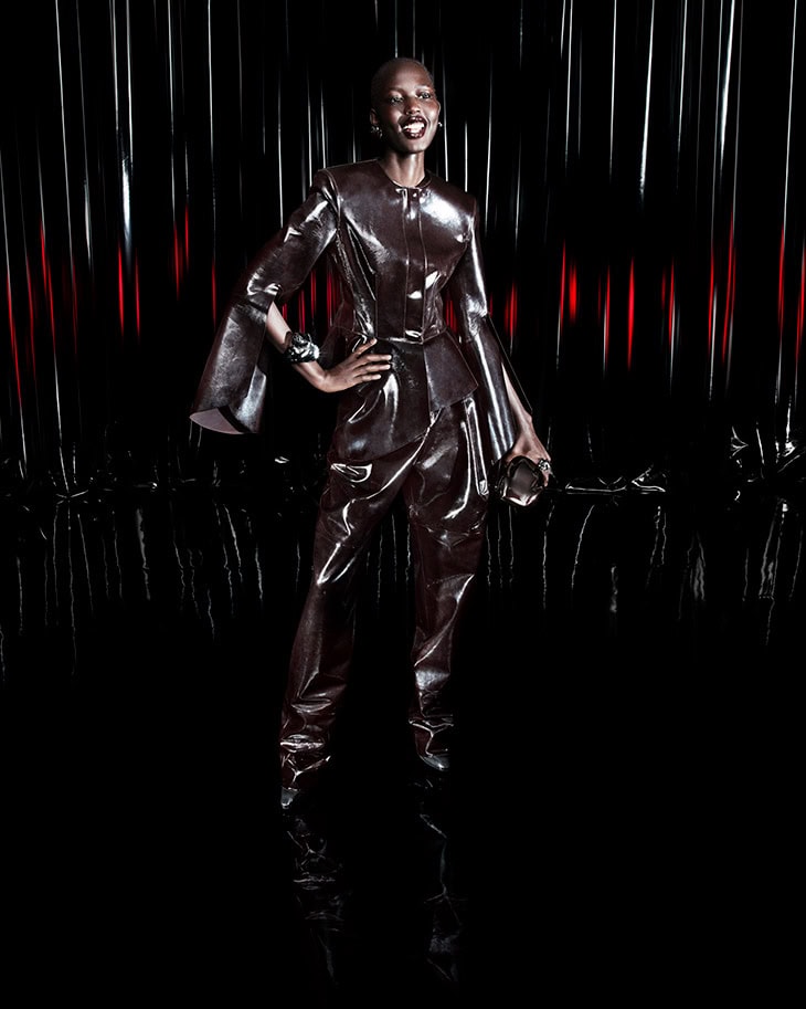 Model Nyaduola Gabriel wearing glossy brown leather outfit against dark background for Ferrari ad campaign.