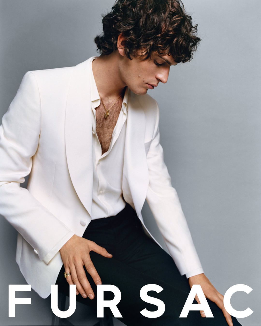 Model wearing a white blazer and black trousers against a grey studio backdrop for Fursac Fall 2024 ad campaign.