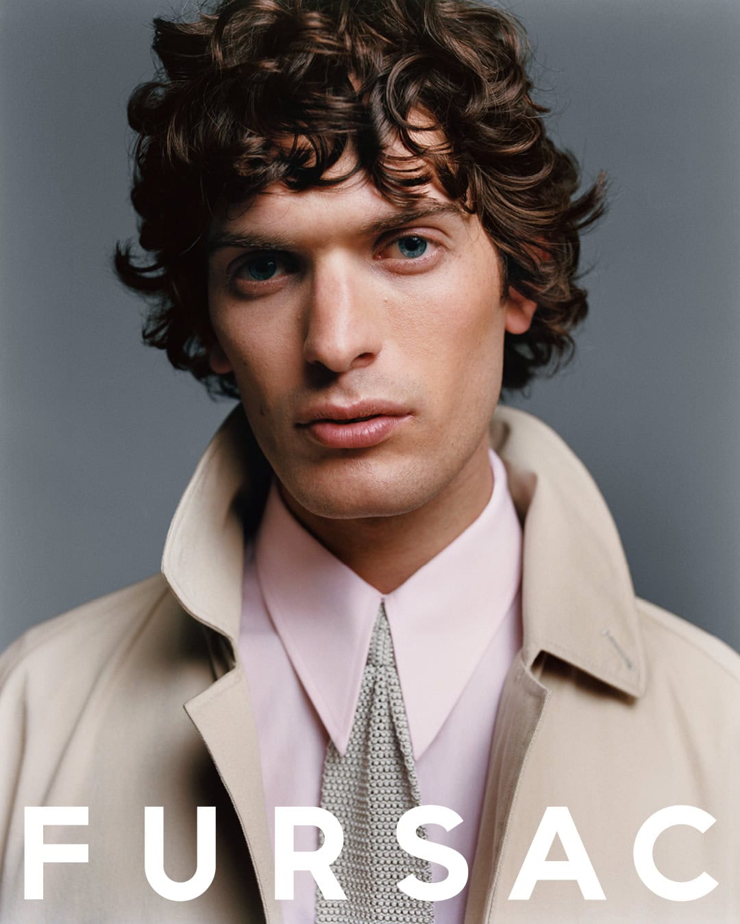 Portrait of a man with curly hair wearing a beige jacket, pink shirt, and knit tie for Fursac