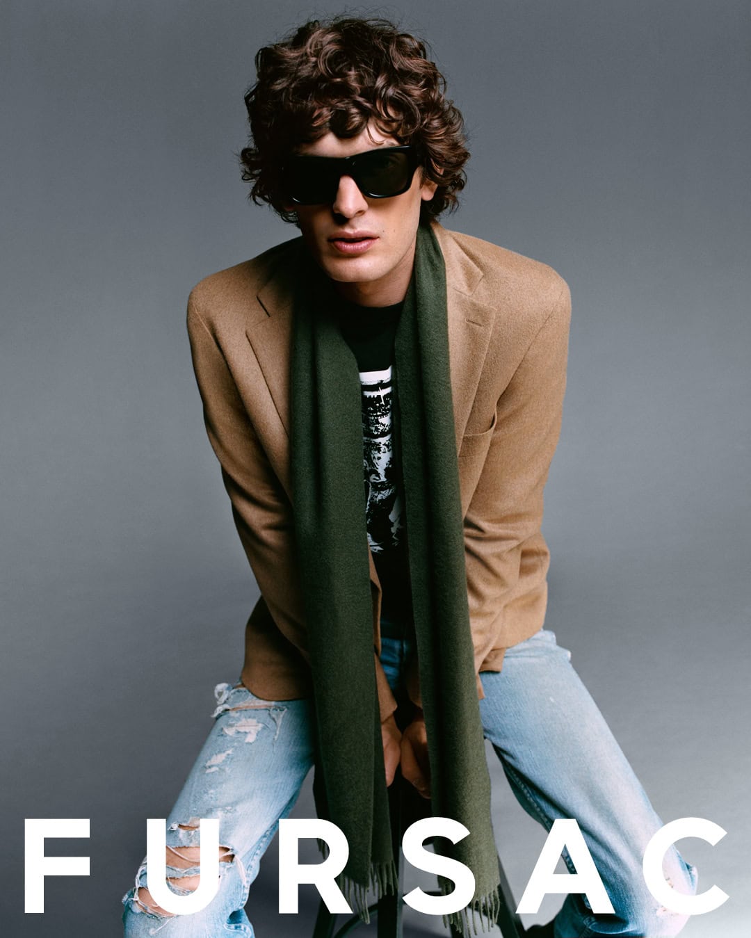 Model wearing a tan blazer and green scarf with distressed denim against a grey backdrop for Fursac.