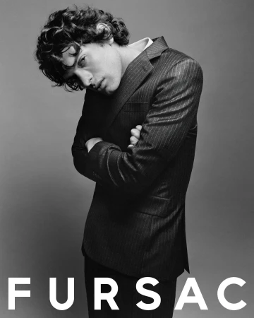 Model with dark curly hair wearing a pinstripe suit jacket with crossed arms against a neutral studio backdrop