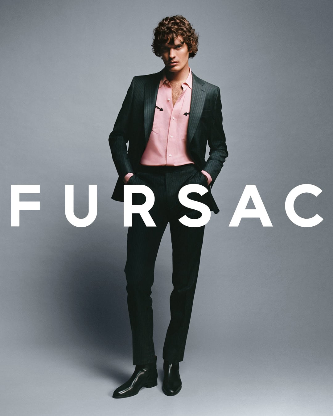 Model wearing a dark pinstripe suit over a pink western shirt against a plain grey background with large white brand text overlay.