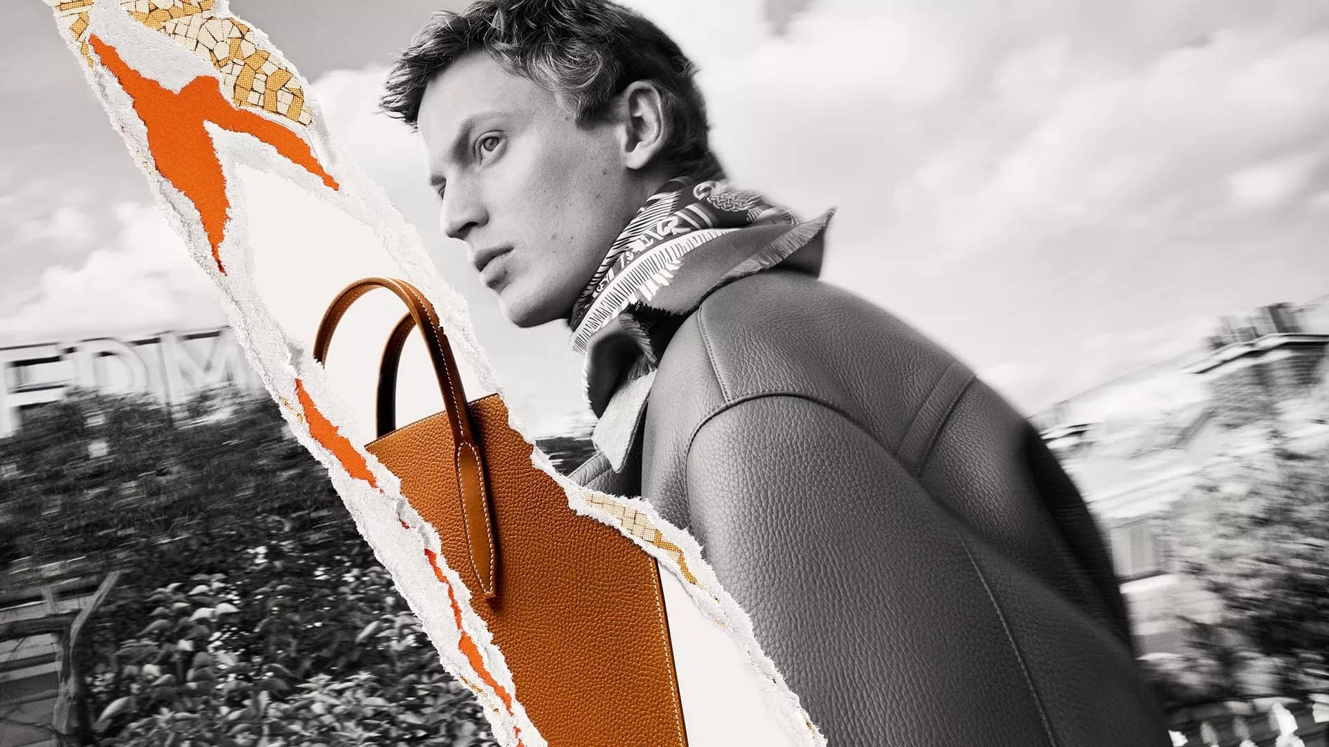 Monochrome fashion advertising image featuring a male model wearing a patterned scarf and leather jacket alongside a textured orange leather bag.