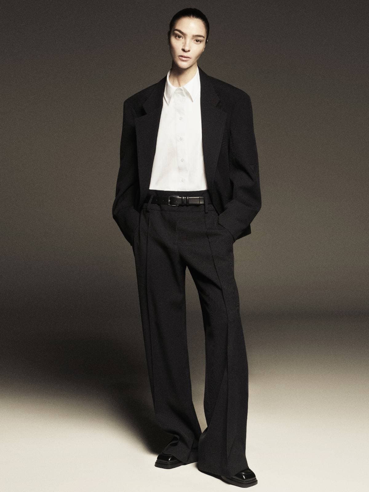 Model wearing a black tailored blazer, white button-down shirt, and black trousers against a neutral studio backdrop