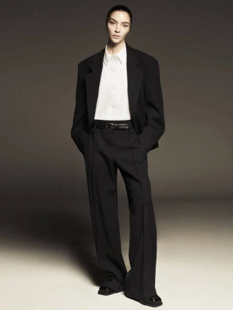 Model wearing a black tailored blazer, white button-down shirt, and black trousers against a neutral studio backdrop