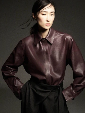 Model wearing a deep burgundy leather shirt and dark skirt posing against a neutral grey studio backdrop