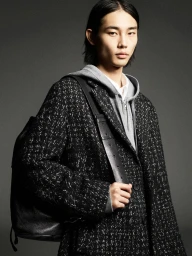 Model Taemin Park wearing a black tweed coat and grey hoodie holding a leather backpack for COS Fall 2024 ad campaign