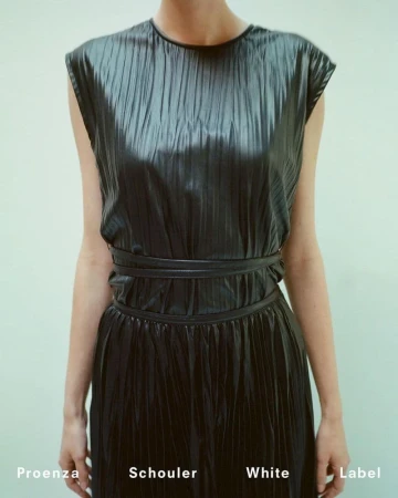 Model wearing a sleeveless pleated black dress with thin waist ties against a light seamless background for Proenza Schouler