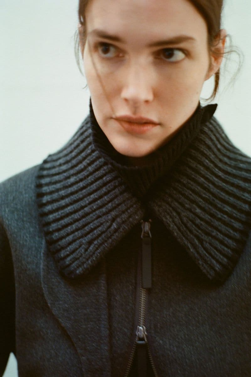 Close-up portrait of model Vanessa Moody wearing a dark ribbed-collar coat against a plain light background