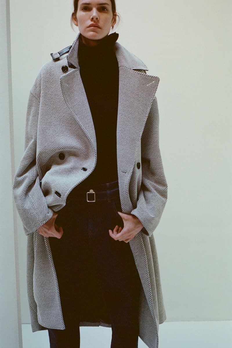 Model Vanessa Moody wearing a patterned grey oversized coat and dark trousers against a plain studio background.