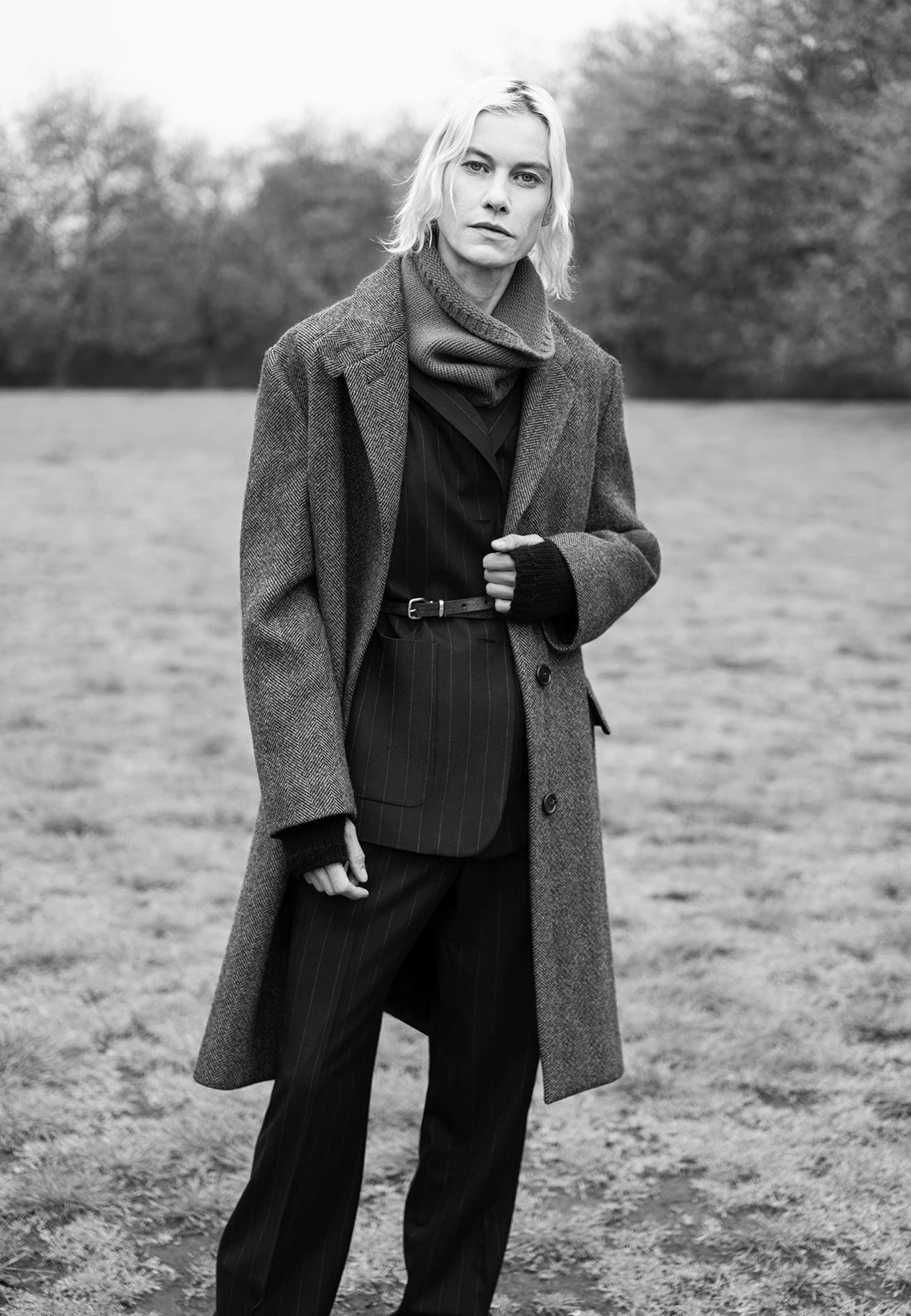 Monochrome portrait of a model wearing a heavy wool coat and scarf outdoors in a park.