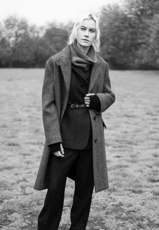 Monochrome portrait of a model wearing a heavy wool coat and scarf outdoors in a park.