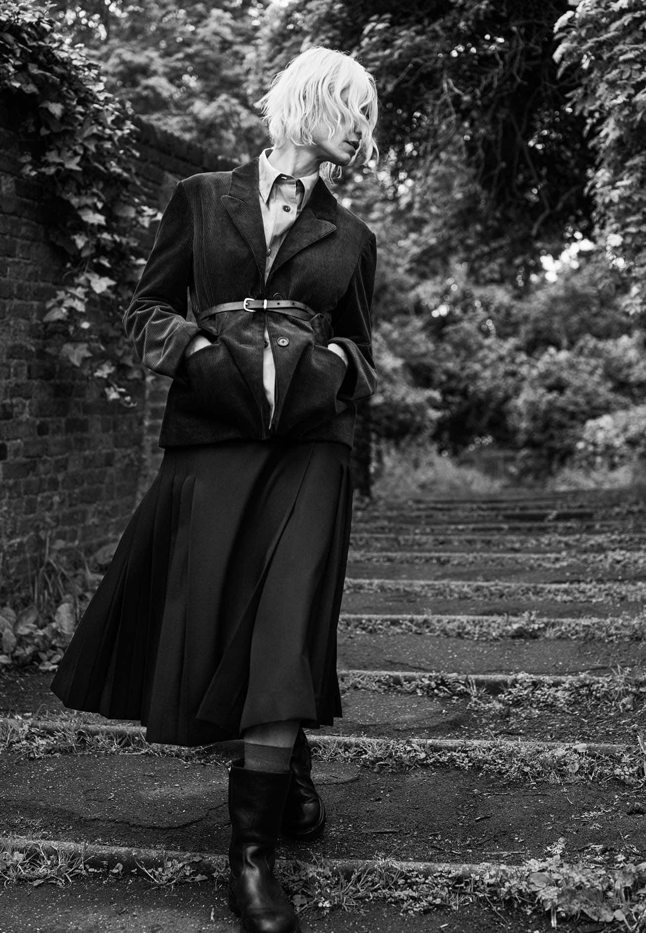 Black and white portrait of a blonde woman wearing a tailored blazer and pleated midi skirt outdoors in London