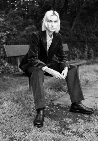 Model wearing a dark velvet blazer and trousers seated on a park bench outdoors