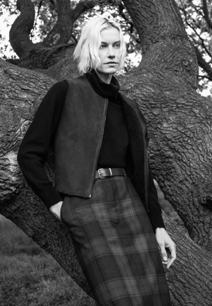 Model with blonde hair leaning against a large tree wearing a dark turtleneck and patterned skirt for Margaret Howell.