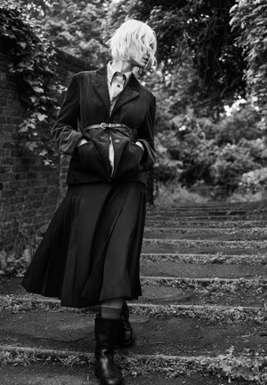 Black and white portrait of a blonde woman wearing a tailored blazer and pleated midi skirt outdoors in London